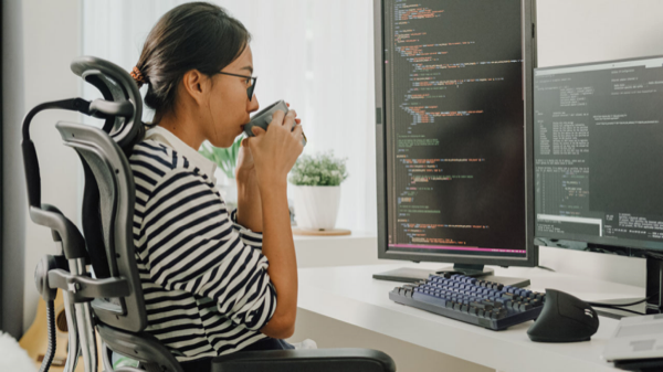 Developer drinking coffee while reviewing code on dual monitors.